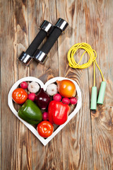 Sport and diet. Vegetables  dumbbells. Peppers, tomatoes, garlic, onions,  radishes in the heart on rustic background