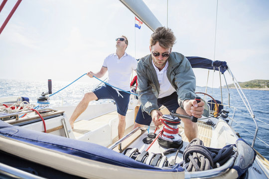 Two men turning cable winch on sail ship