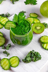 Fresh Green smoothie with kale, cucumber, lime, apple, parsley on white board.
