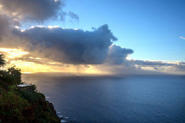 sunset on the sea coast. The ocean, vegetation, clouds, illuminated by the sun and the rain