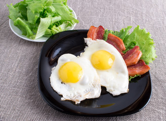 Black plate with fried eggs, bacon and lettuce