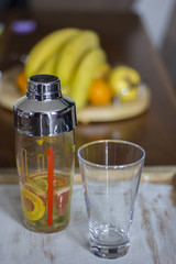    kiwis, grey fruits and oranges together with a shaker and a glass on a dark lit background.