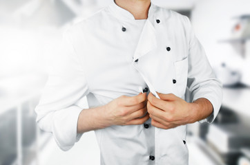 Obraz na płótnie Canvas Chef buttoning his uniform on the kitchen background.