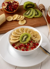 Healthy oatmeal porridge with fruits in white bowl on wooden table.