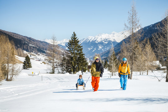 Family pulling sledge with son in Alpine winter scenery