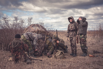 Hunters preparing for team hunting in rural field with hunting tent in overcast day