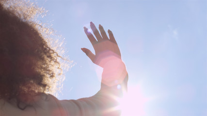 Female hand touching blue sky and raising to sun.