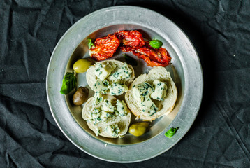Flat lay of Spanish tapas sandwich with blue cheese roquefort, olives, sun dried tomatoes, and basil against back background