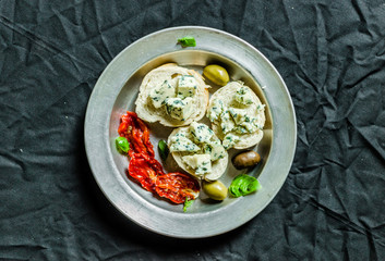 Flat lay of Spanish tapas sandwich with blue cheese roquefort, olives, sun dried tomatoes, and basil against back background