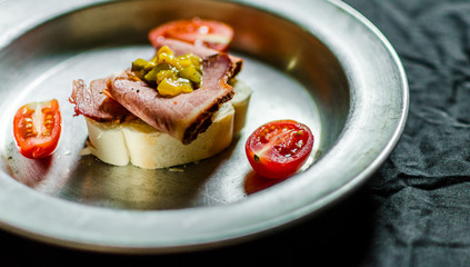 Close up of a Jewish appetizer sandwich with pastrami, mustard relish, and cherry tomatoes. Selective focus