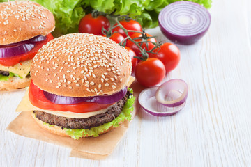 Homemade cheeseburger on white wooden surface.