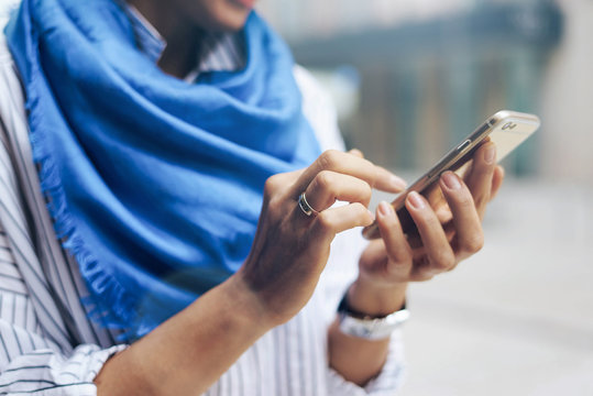 Close up photo of woman's hands touching the screen of a modern mobile phone while standing on a blurred street background. Hipster girl is typing e-mails on her smartphone using wi-fi connection