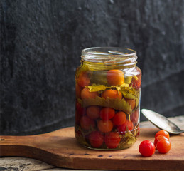 Marinated cherry tomatoes in an open glass jar and put some tomatoes next to a jar on wooden board on a dark background

