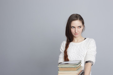 girl with long hair holding a pile of books and looking away.