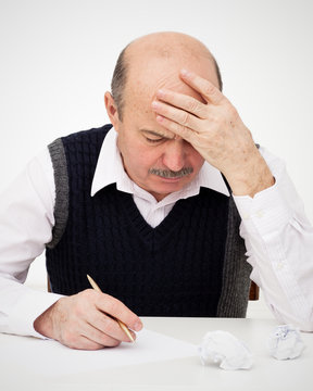 Elderly man writes, draws something on a piece of paper, to fill in an application or a will. Think of the solution to the problem or a difficult task