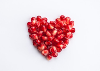 Heart shaped pomegranate seeds on white background. Love, Valentines day and healthy life concept, flat lay top view