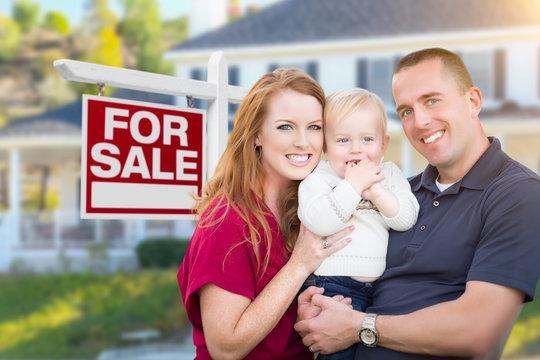 Happy Young Military Family in Front of For Sale Real Estate Sign and New House.
