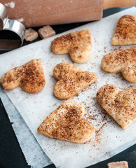 Baking background with Valentines day heart shaped cookies with brown sugar and cinnamon, rolling pin on kitchen black table, Valentines day dessert cooking concept