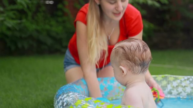 Happy young mother playing with her 1 year old son in inflatable swimming pool