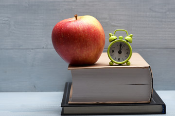 Books, red apple and alarm clock