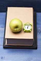 Books, green apple and alarm clock