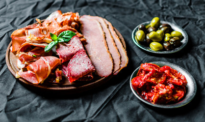 Close up of Italian cold meat antipasti delicatessen platter against black background. Selective focus
