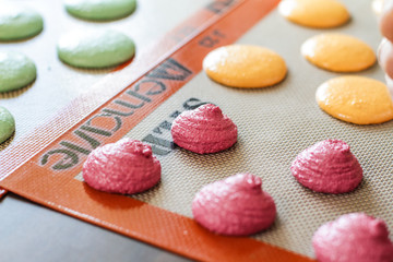 Piping out red macaron mixture on to the baking tray