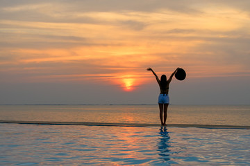 Woman holding hat relaxing at the pool on the sunset and twilight