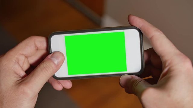 A man uses a blank green screen smartphone to play a video game. 