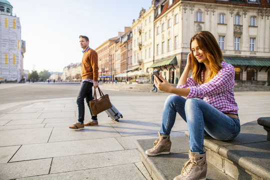 Mid adult woman using smart phone with man in background