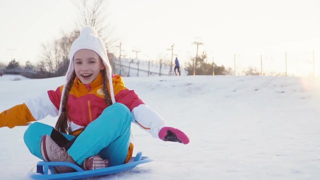 Child rides a sledding down on snow disk a winter hill at camera. Girl smiling at camera. Slow Motion from Sony a6300