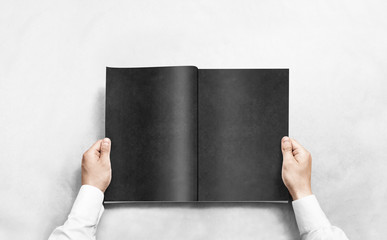 Hand opening black journal with blank pages mockup. Arm in shirt holding grey magazine template...