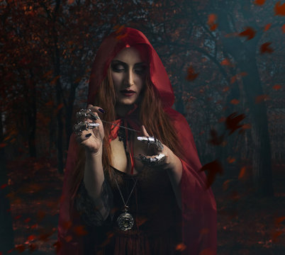 Sorceress in the forest. Beautiful sexy sorceress in red cloak holding antique clock watch standing in the forest photo.