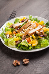 Orange Walnut Chicken Salad  on a white plate with  dark wooden background topped with orange vinaigrette dressing