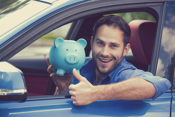 Man sitting inside new car holding piggy bank showing thumbs up