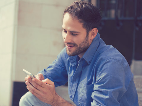 Happy man texting on phone sitting on stairs outside office