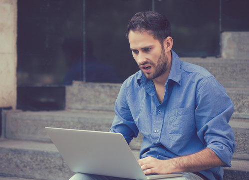 worried man working on laptop computer sitting outdoors