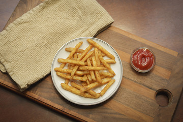 A plate of french fries with ketchup on a wooden cutting board