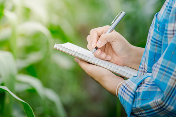 Woman's hand take notes with a pen on a notebook in agriculture garden.
