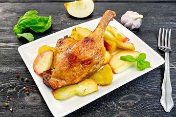 Duck leg with apple and basil in plate on board