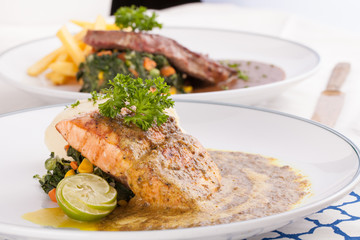 A decorating nice dish of salmon steak and beef served with mashed potato,lemon, saute spinach and sauce on background with wooden utensils.