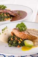 A decorating nice dish of salmon steak and beef served with mashed potato,lemon, saute spinach and sauce on background with wooden utensils.