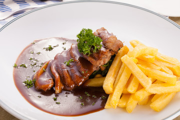 A nice dish of roasted duck breast confit in orange sauce served with fries on the table
