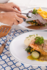 A female hand using knife cutting beef steak decorated with fries in a nice dish set on a table.
