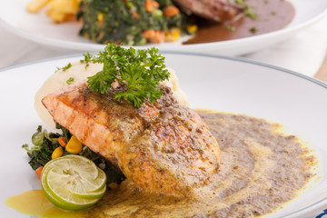 A decorating nice dish of salmon steak and beef served with mashed potato,lemon, saute spinach and sauce on background with wooden utensils.