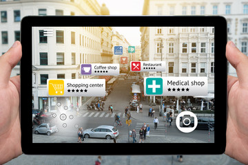 Augmented reality marketing technology concept. Hand holding tablet use AR application to check relevant information about the spaces around customer. City and flare light background