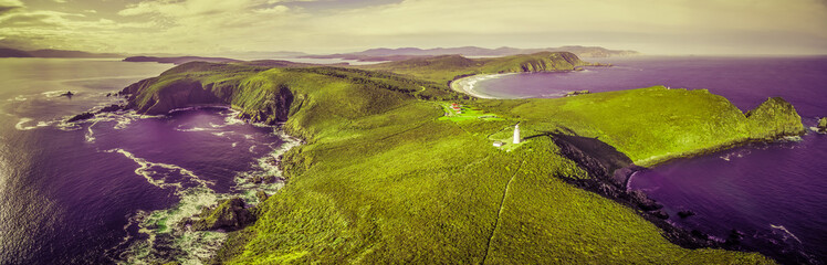 Surreal aerial landscape of ocean, land, and lighthouse in vivid green and purple colors