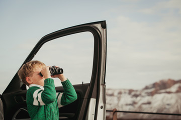 little boy looking through binoculars travel by car in mountains