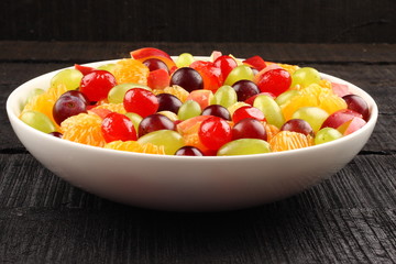 Fresh summer fruit bowl in black wooden background,
