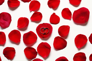  Two golden wedding rings is in red rose petals on a white wooden table